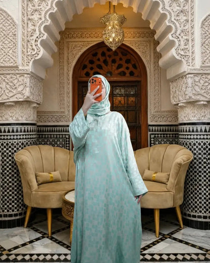 Woman in a light blue dress taking a selfie in a decorative room with arches and patterned tiles.