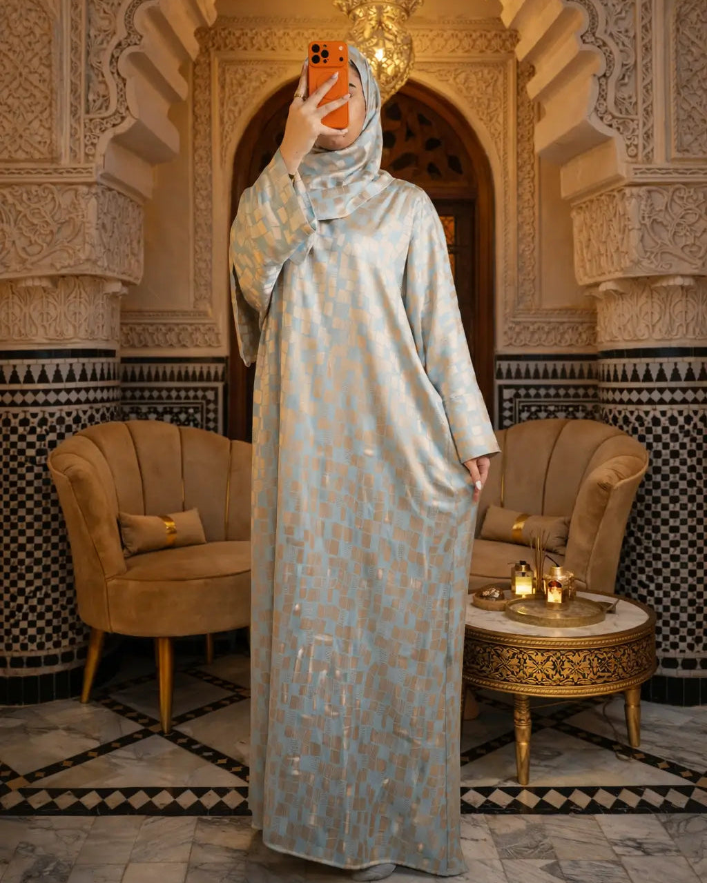 Woman in a long, light-colored dress standing in an ornate room with decorative arches and furniture.
