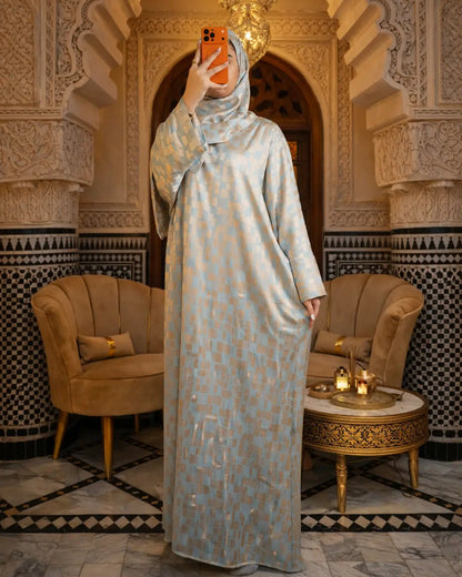 Woman in a long, light-colored dress standing in an ornate room with decorative arches and furniture.